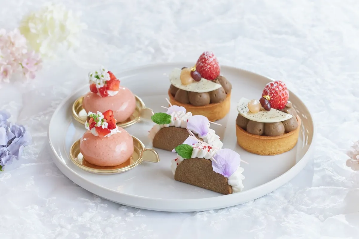 ピンク色のムース、イチゴを乗せたチョコタルト、紫の花びらを添えたほうじ茶スイーツが並ぶプレート