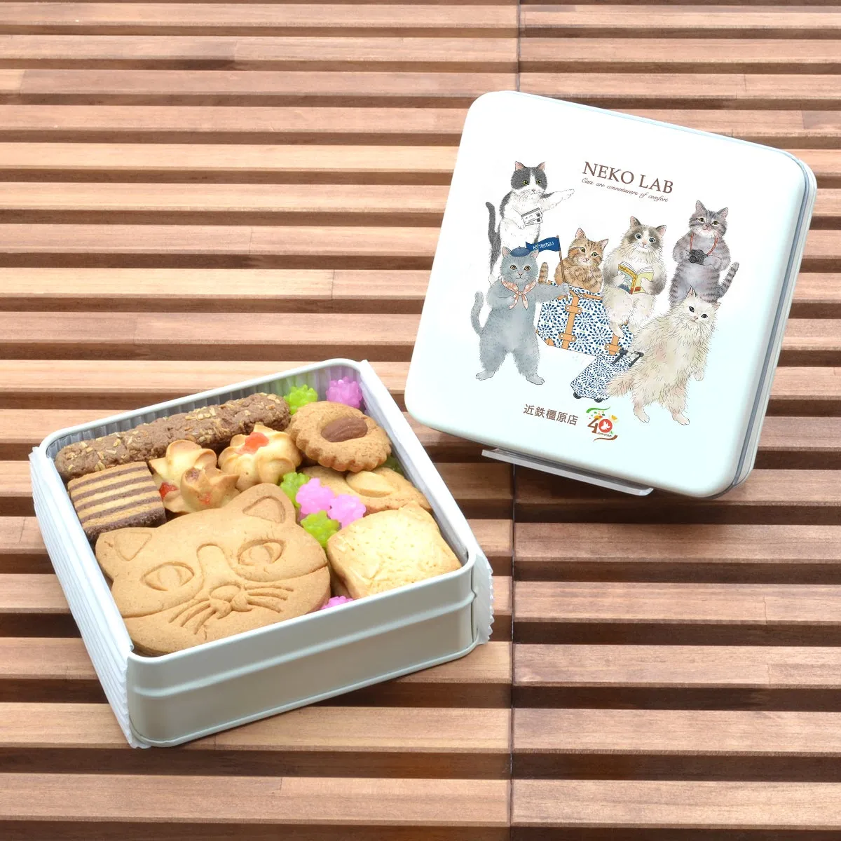 近鉄橿原店40周年限定のクッキー缶。蓋には旅の準備をする猫たちが描かれ、中には大きな猫顔クッキーや彩り豊かな焼き菓子、金平糖が詰まっています。