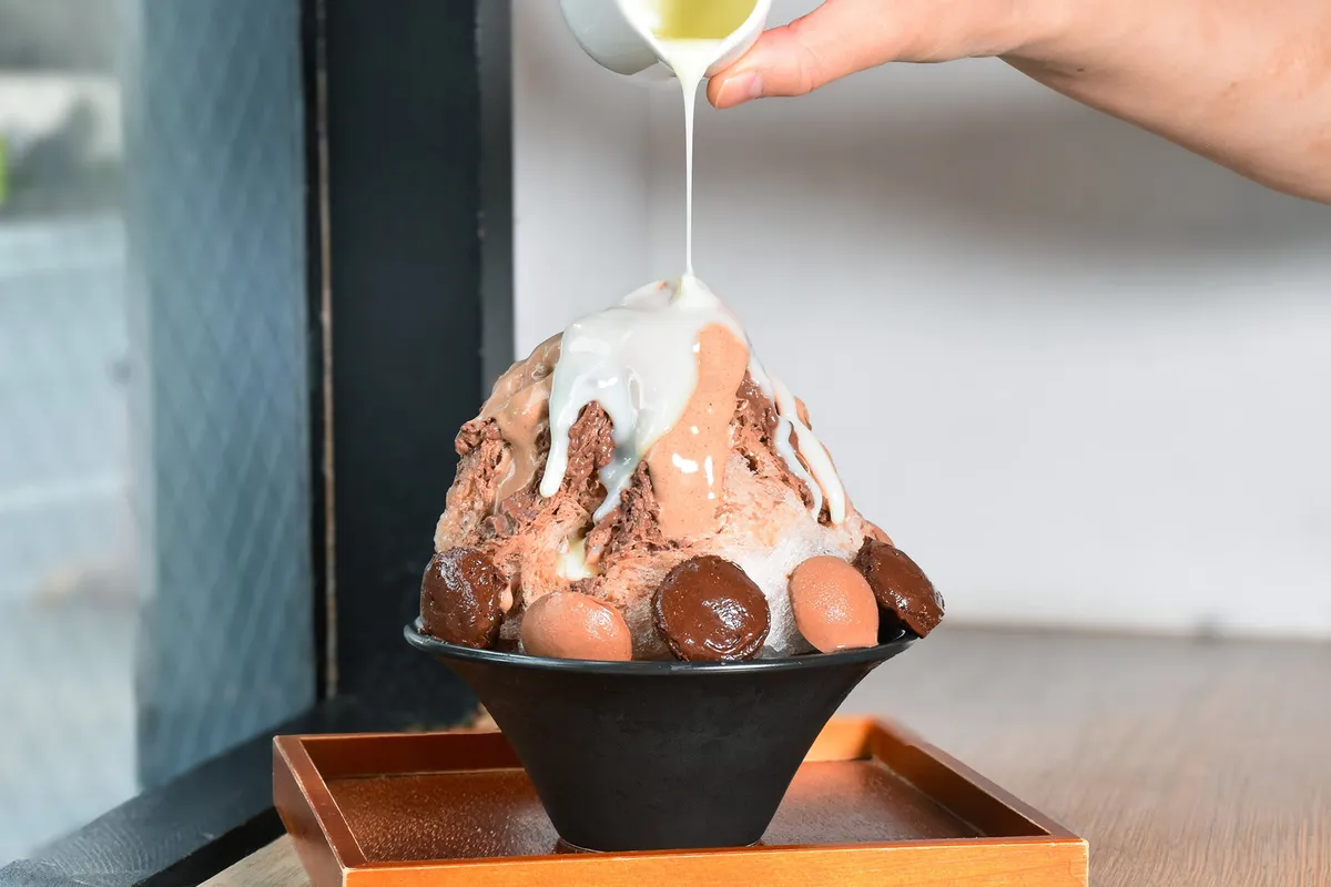 チョコレートかき氷にミルクソースをかける様子