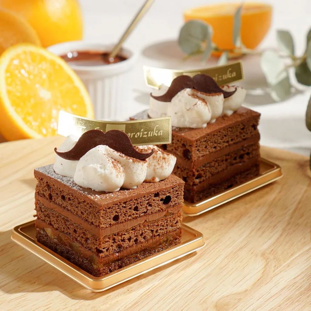 グラティチュードのカットケーキ。層の美しさが際立ち、トップにはクリームとヒゲ型のチョコレートが飾られています。