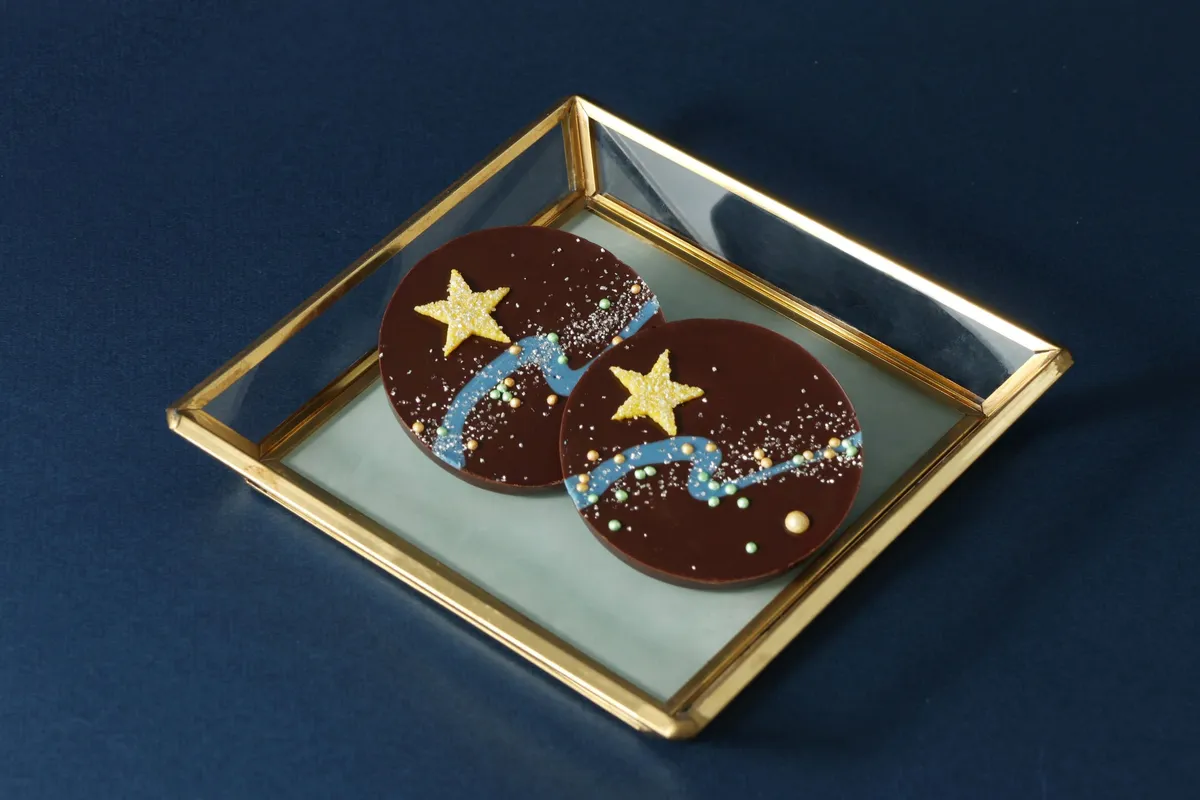 ダークチョコの上に青いラインと黄色い星が描かれた丸いパレショコラ