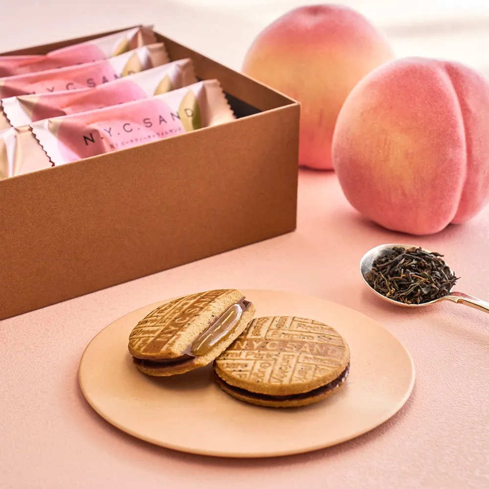 新作ピーチティーキャラメルサンドのパッケージと、背後に置かれた大きな桃、そしてスプーンに盛られた紅茶の茶葉