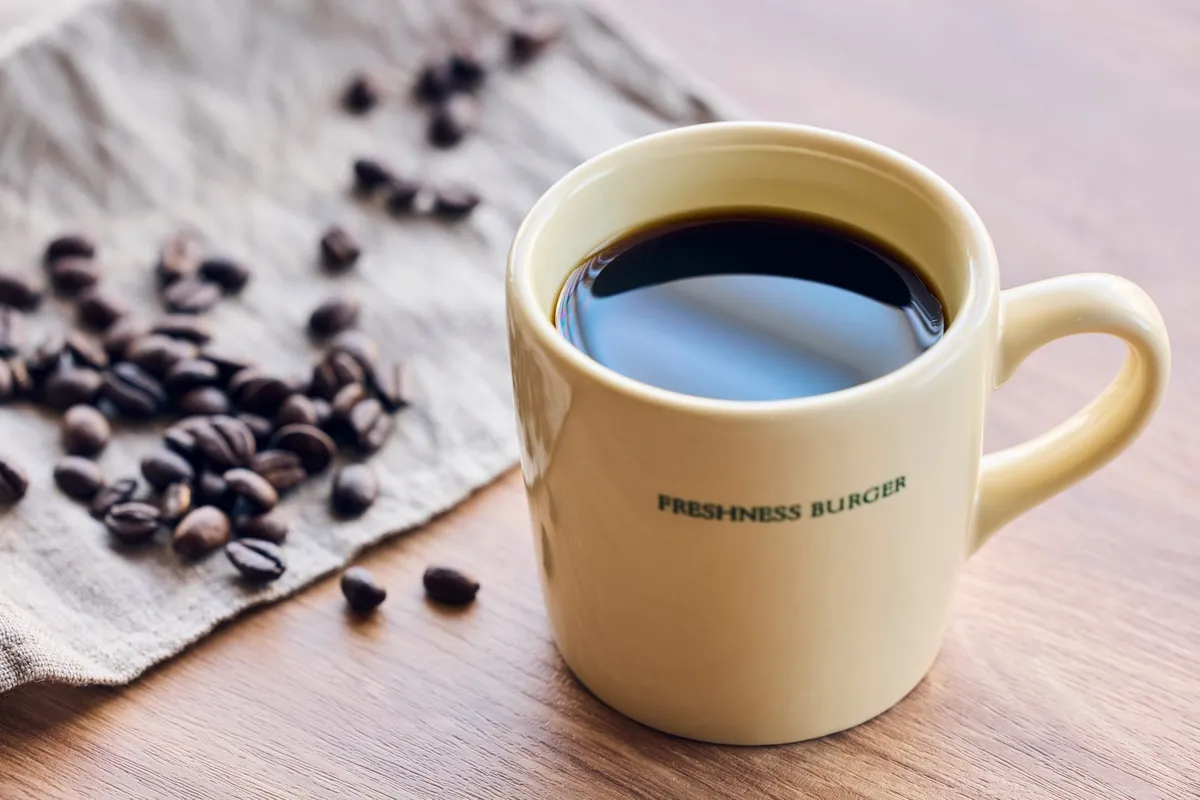 温かいコーヒーが入ったロゴ入りマグカップとコーヒー豆